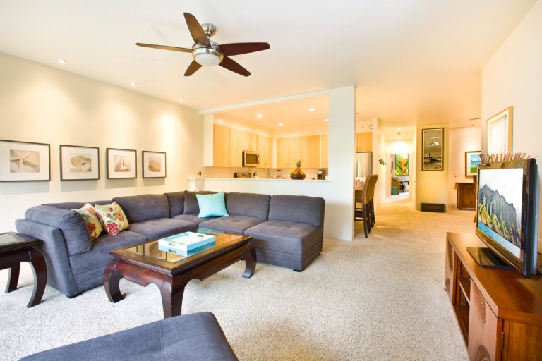 A classic tropical beach themed living room with white painted walls, gray couches, and a ceiling fan with wooden blades, Should A Ceiling Fan Go Clockwise In Summer?