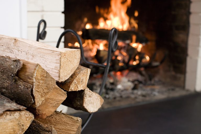 A close up photo of chopped firewood next to a fireplace, Can You Put Too Much Wood In A Fireplace?