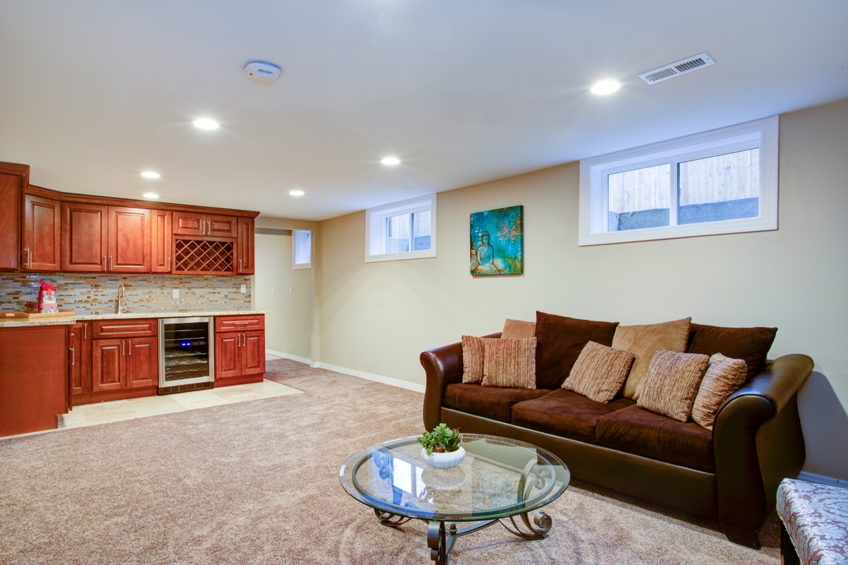 A modern basement with cream colored walls, wooden cabinets, and a brown sleeper couch