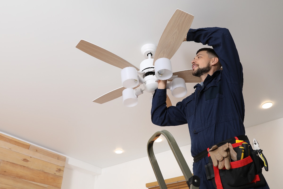 Electrician repairing ceiling fan with lamps