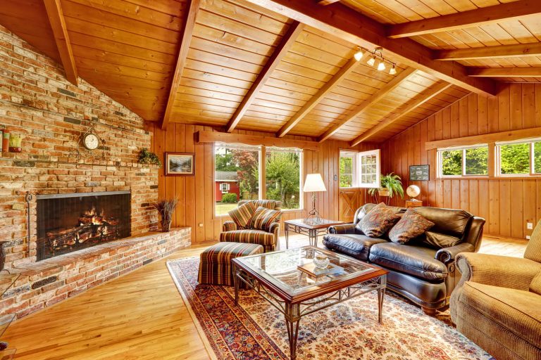 A cozy and warm rustic log cabin with brick mantled fireplace and a huge rug under the furniture's, How To Insulate A Vaulted Ceiling