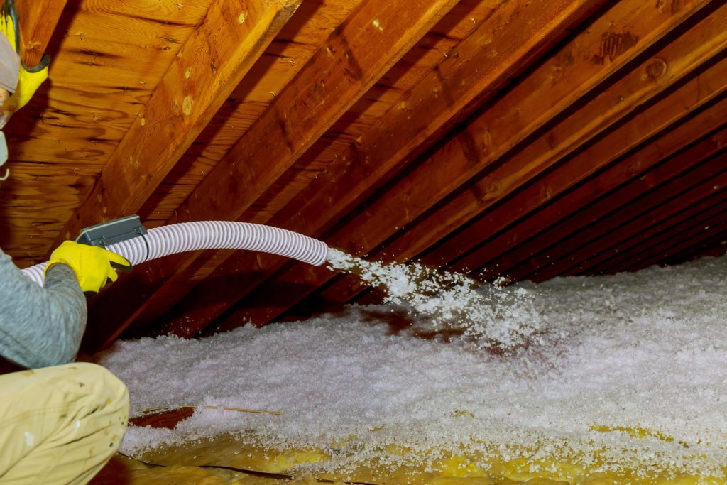 A ventilation worker spraying fiberglass insulation on the attic