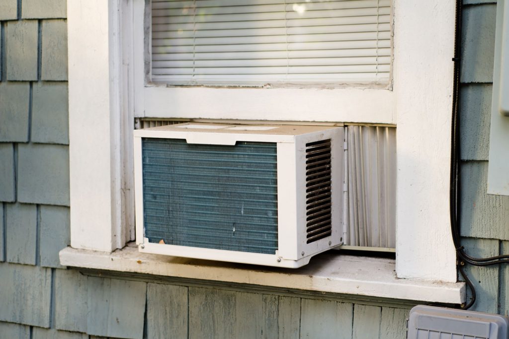 A window air conditioning unit photographed outside a weathered shingle siding house