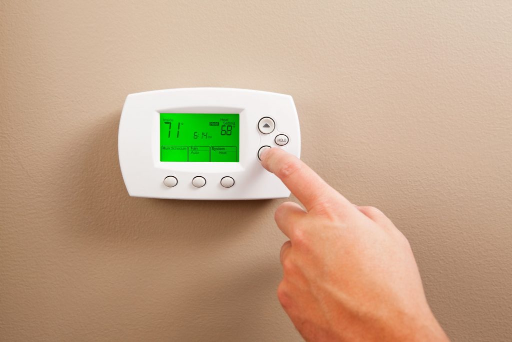 A woman adjusting the room temperature on the thermostat