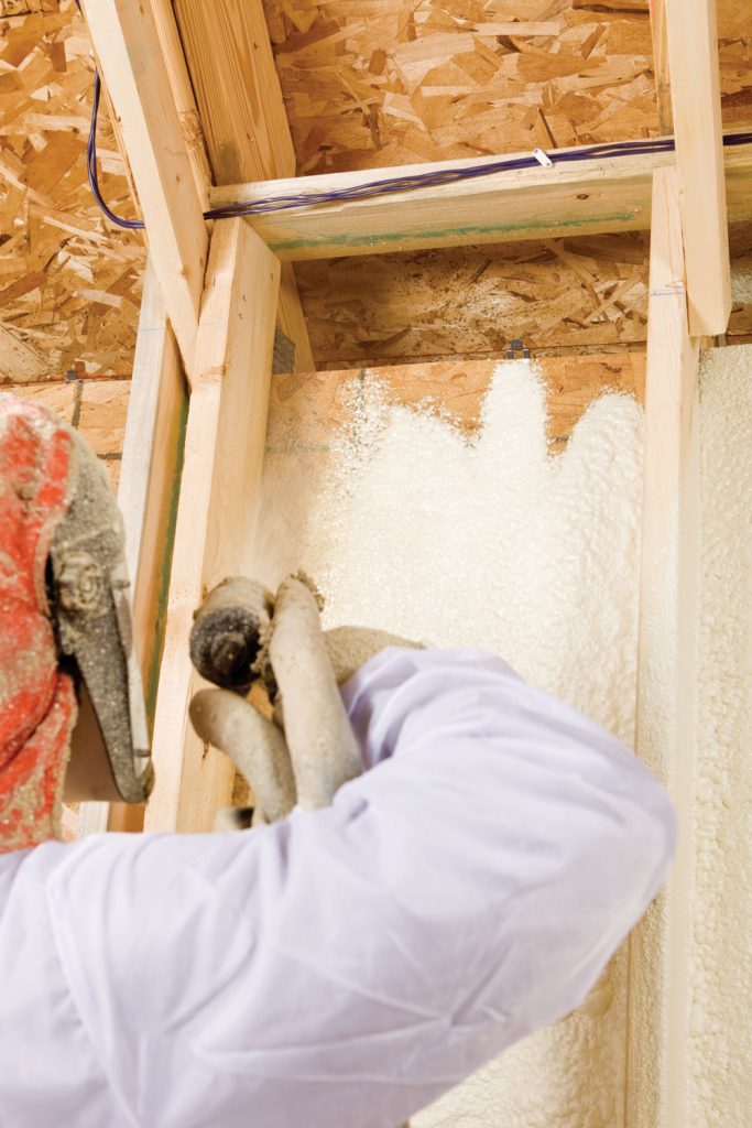 A worker applying foam insulation on the wooden framing 