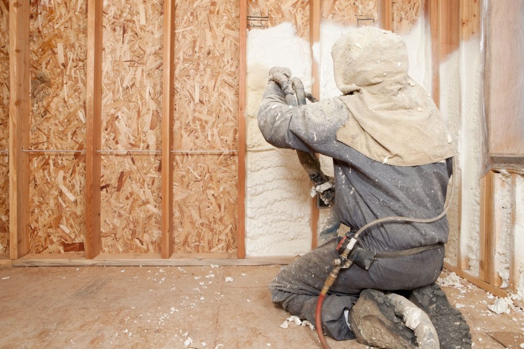 A worker spraying foam insulation in between the wood membranes of a house 