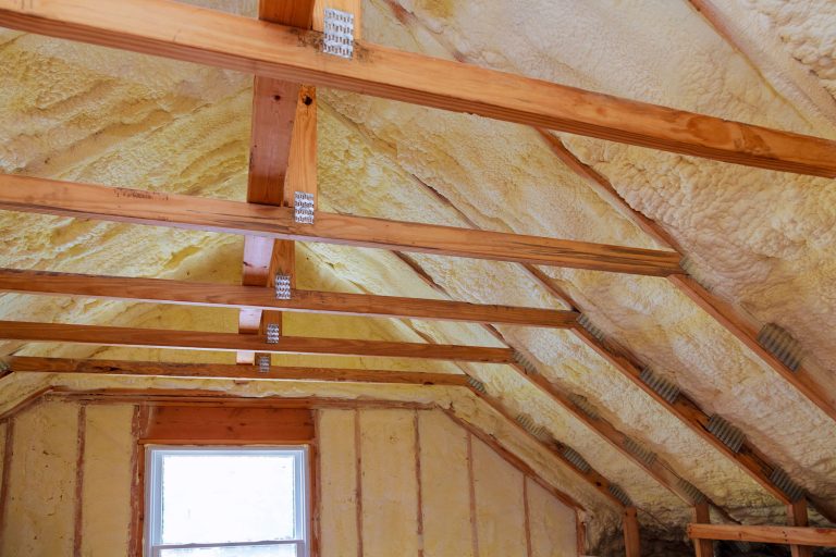 Inner view of an attic of a house with spray foam insulation on the ceiling and walls, How Long Does It Take To Insulate A New House?