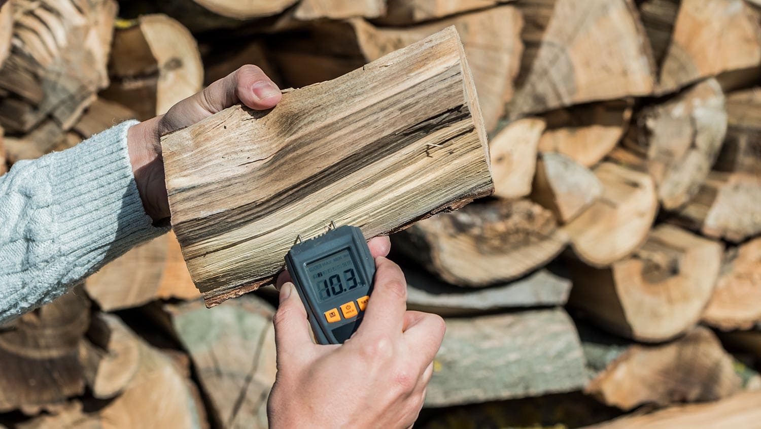 A man measures the humidity of firewood with a moisture meter