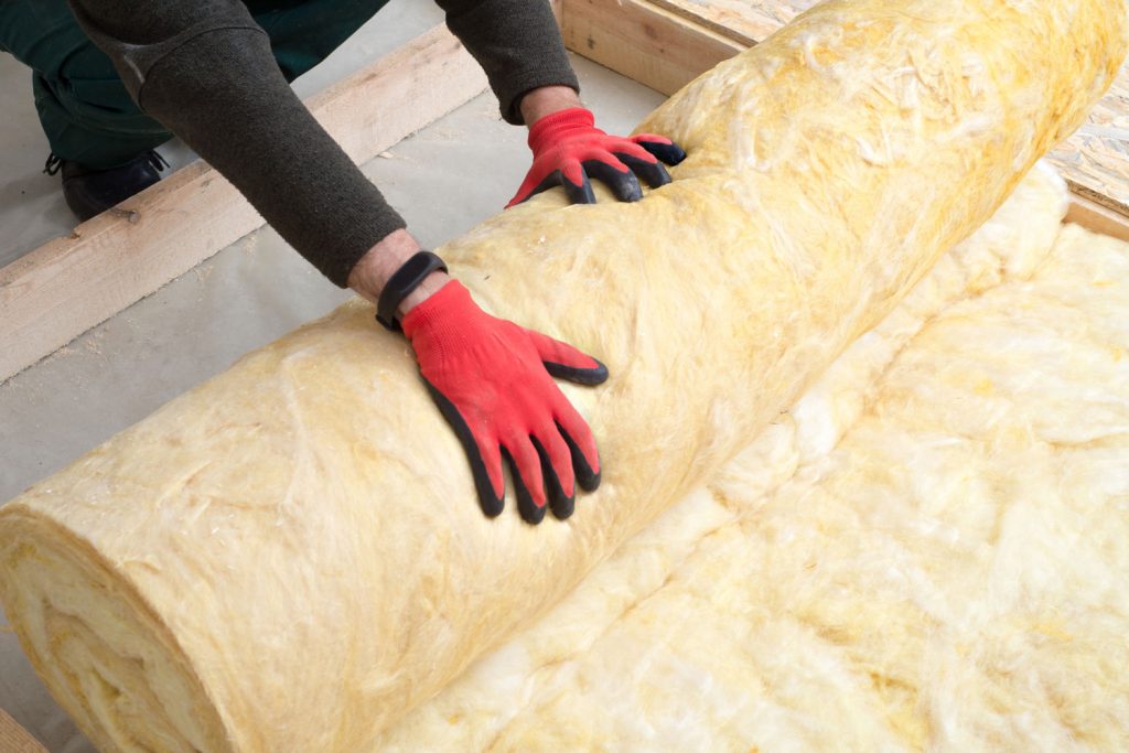 A worker rolling fiberglass insulation in the attic