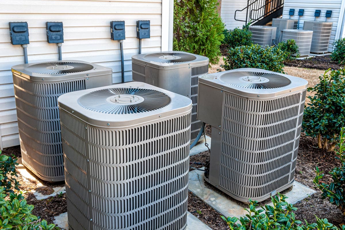 Horizontal shot of four air conditioning units outside of an upscale apartment complex