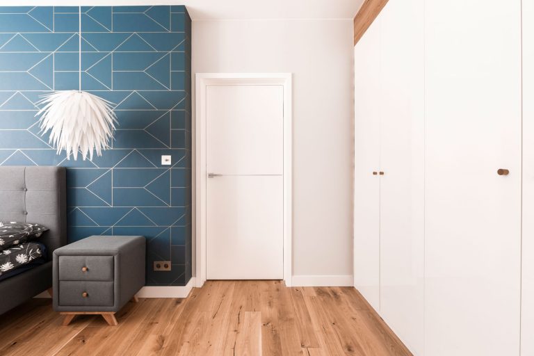 Interior of a modern and Scandinavian themed bedroom with wooden flooring, white walls with a decorative header and white cabinets on the side, Does Closing Bedroom Doors Save Energy?