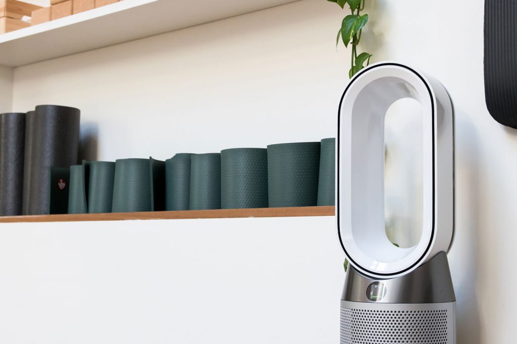 Modern Dyson hot and cool fan heater in a gym interior against a wall with neatly stacked apparatus on shelves in a low angle view, Can You Use A Dyson Fan Outside?