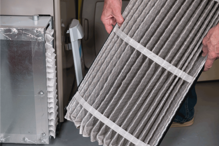 man examining a folded dirty air filter in the HVAC furnace system in basement of home. How Often To Clean Natural Gas Furnace
