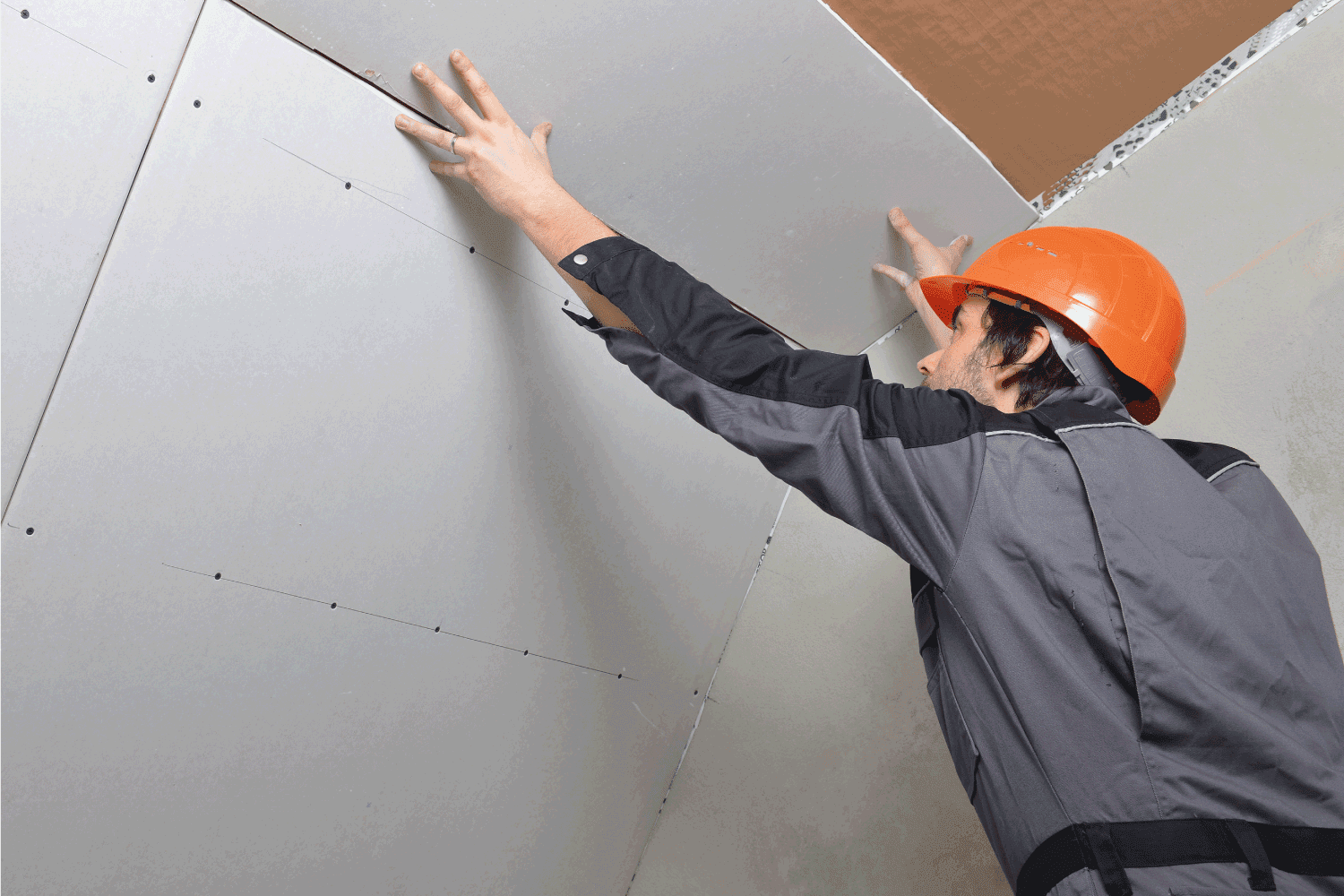 worker installing drywall material against an inclined ceiling