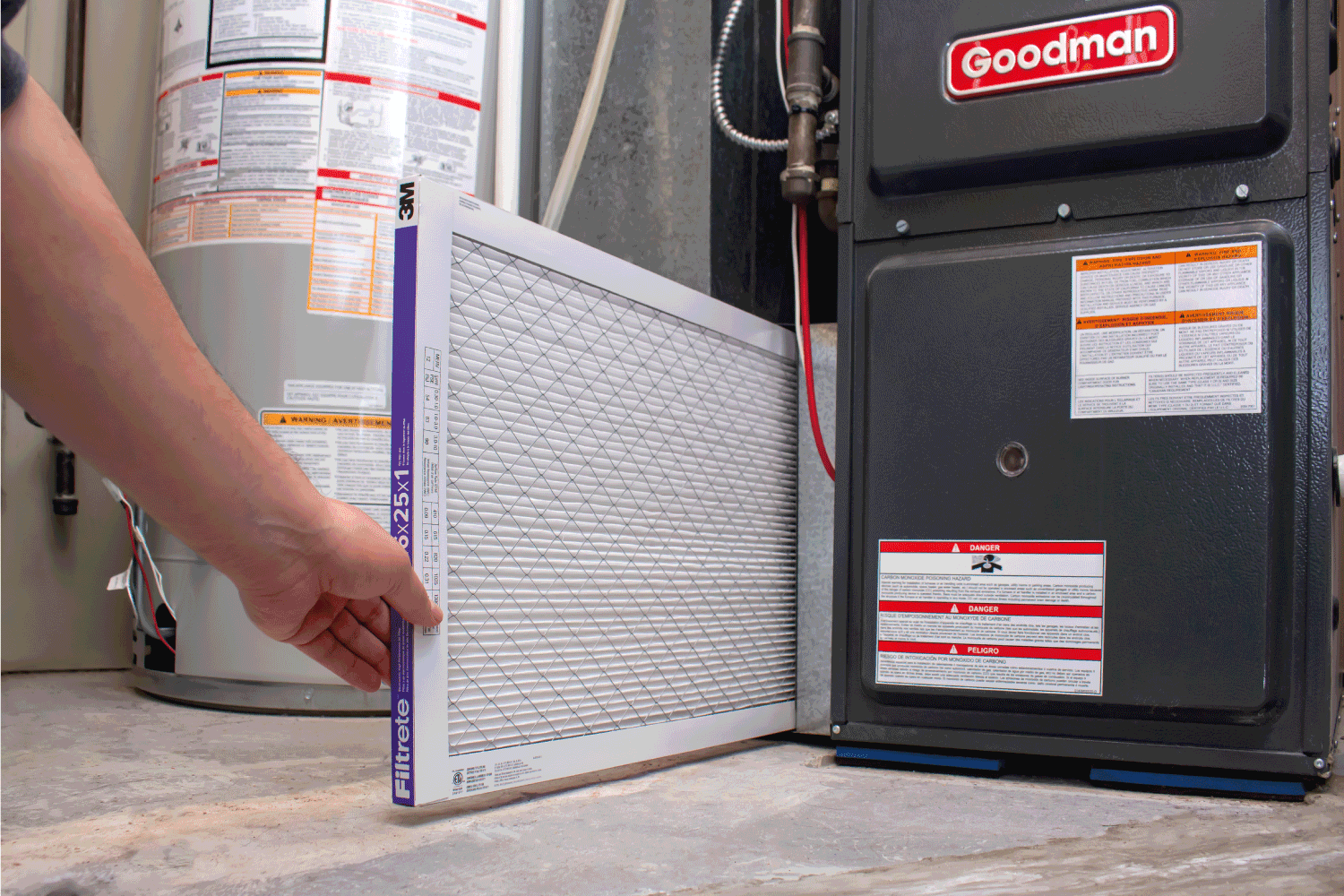 A person changing an clean air filter on a Goodman high efficiency furnace.