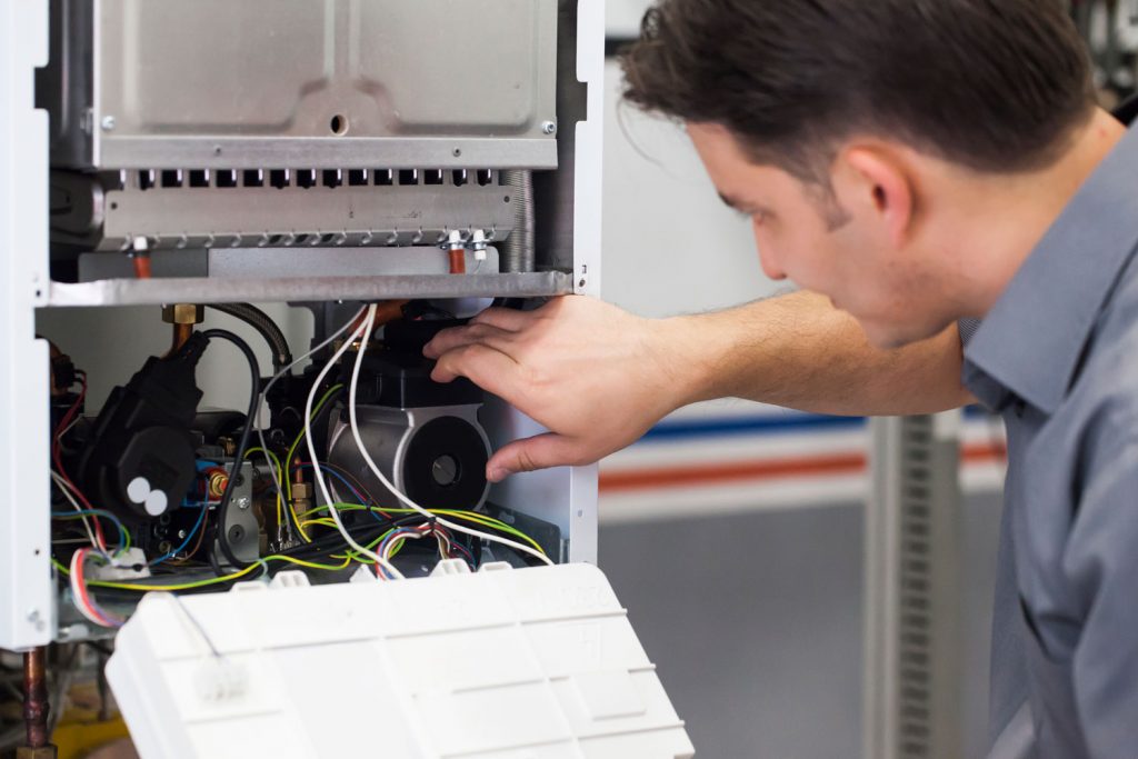 A worker checking the inner components of a gas boiler
