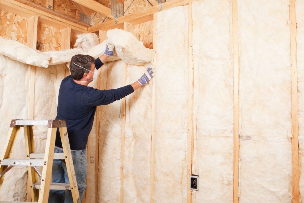 A worker installing fiberglass insulation on the wooden framing of the house