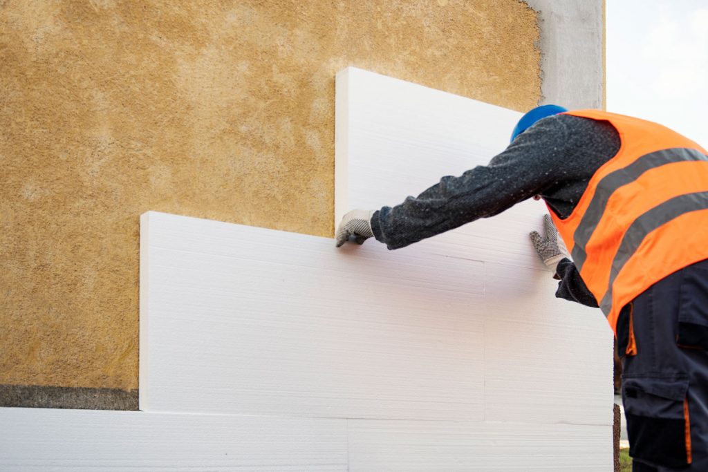 A worker installing foam insulation on the inner walls of a house