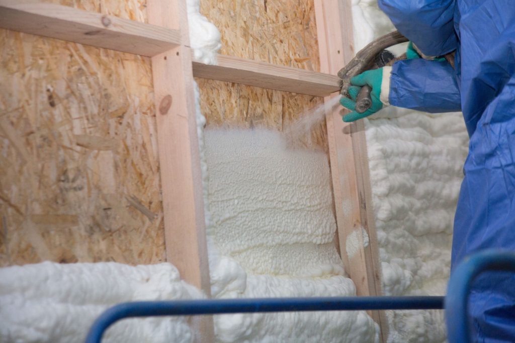 A workman applying fiberglass insulation on the wall framing
