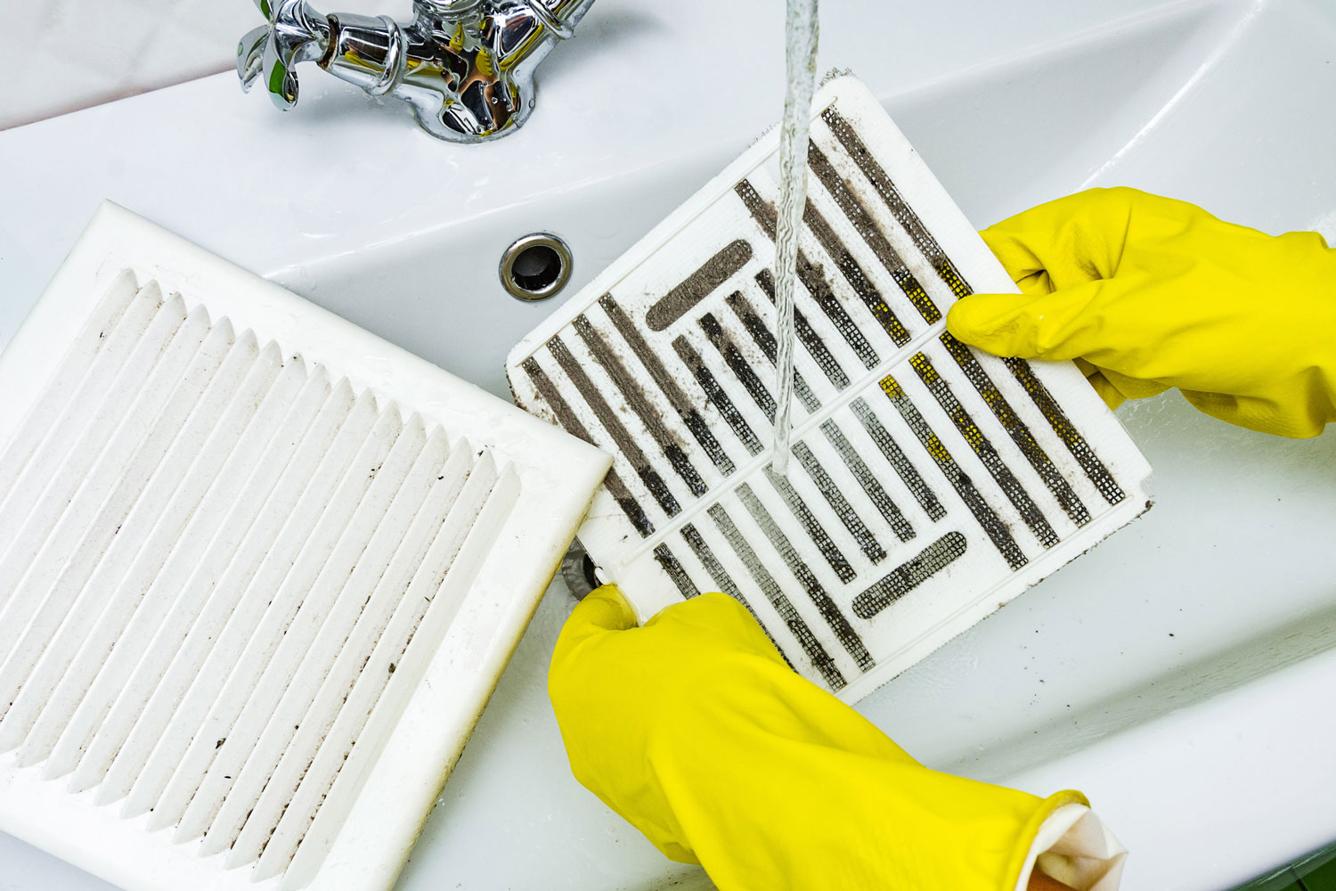 Person in a protective rubber glove washes in the sink air filter of the ventilation return duct blocked by dust and debris