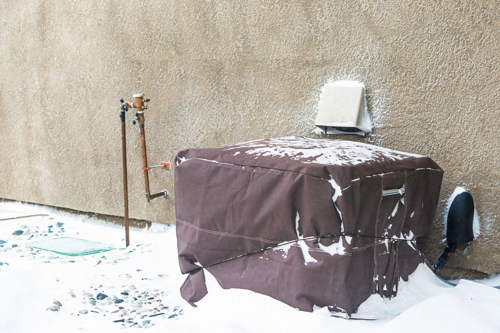 Residential-air-conditioning-unit-wrapped-with-protective-cover-in-blizzard