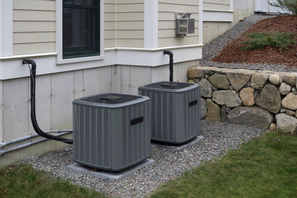 Two central air conditioning units set up outside a single storey house