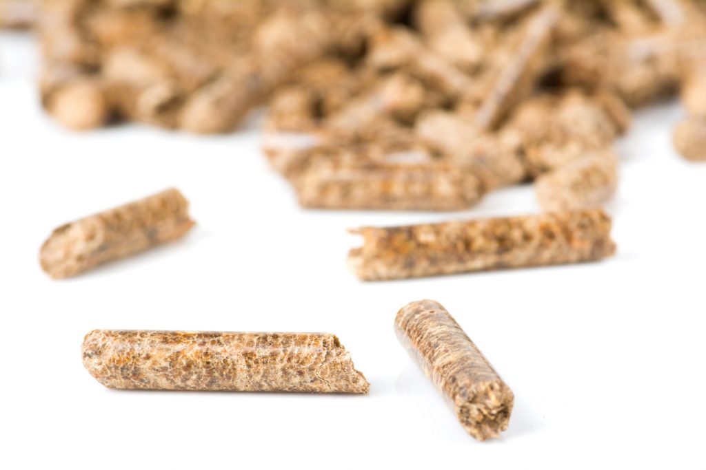 Wood burning pellets, close-up of several wood burning pellets with a stack of wood burning pellets in the background.