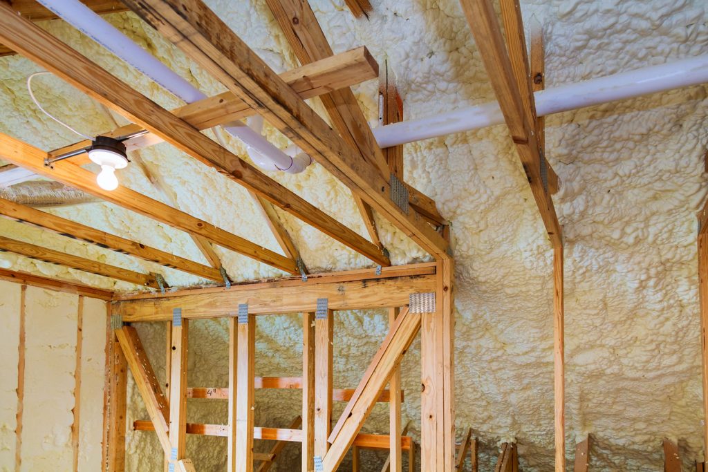 Wooden framing of a house attic insulated with fiberglass insulation with visible electric tubes 