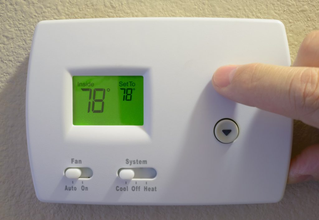 man's hand adjusting home thermostat to energy-saving summer setting of 78 degrees Farenheit (26 Celsius)