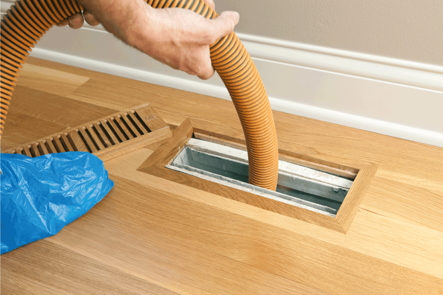 worker is using a shop vacuum to clean a vent and duct on a new hardwood floor