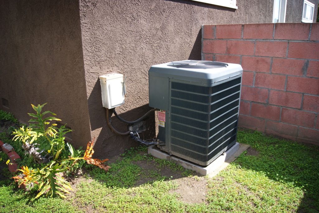 A black colored air heat pump on the side of the house