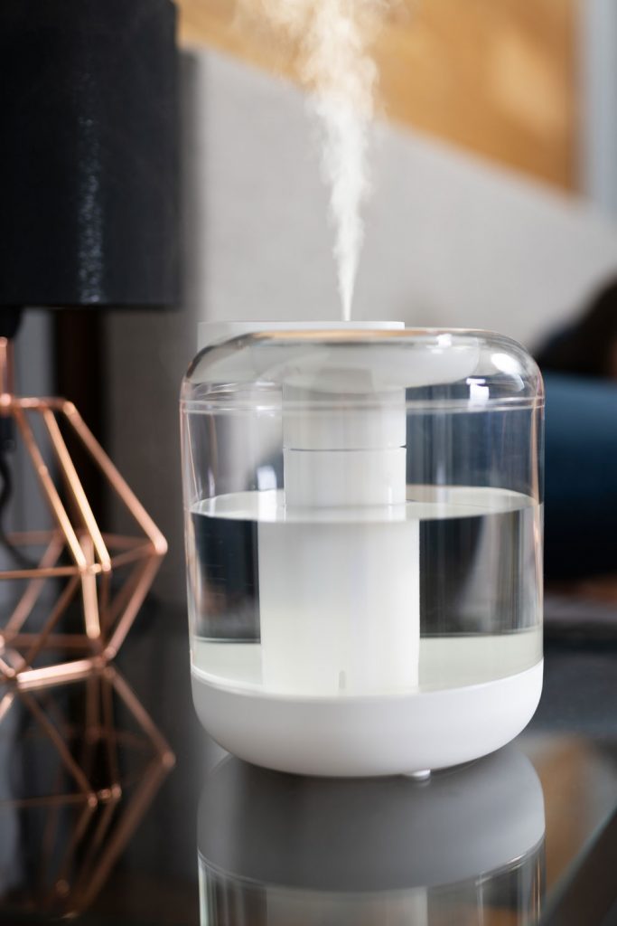A clear glass humidifier placed near the bed
