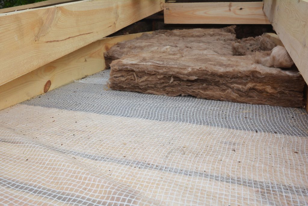 A close-up of roof mineral wool, glass wool insulation over a vapor barrier, membrane between the wooden ceiling joists.