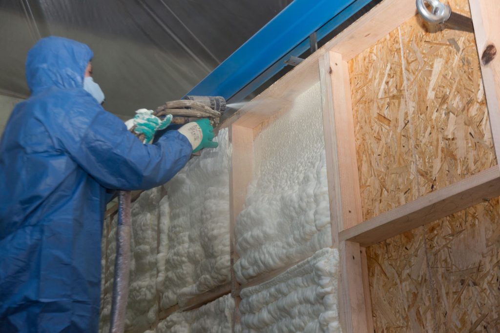 A fully suited Hvac personnel spraying foam insulation on the walls