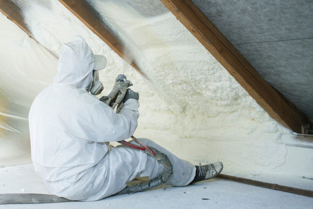 A fully suited insulation specialist spraying foam insulation of the ceiling