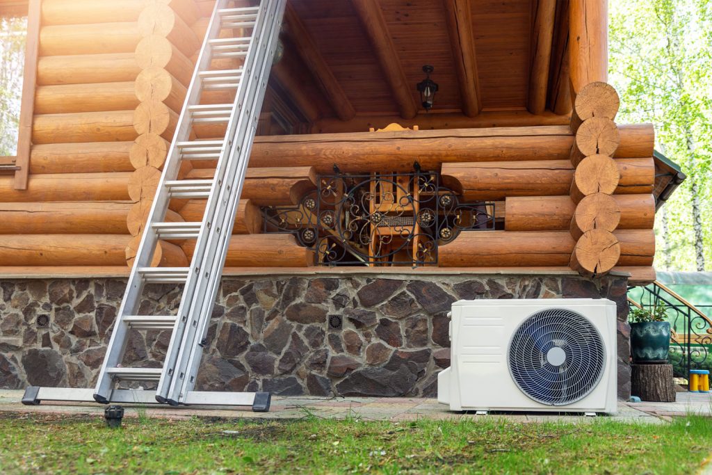 A gorgeous log cabin designed house in the forest with an air heat pump placed near the porch