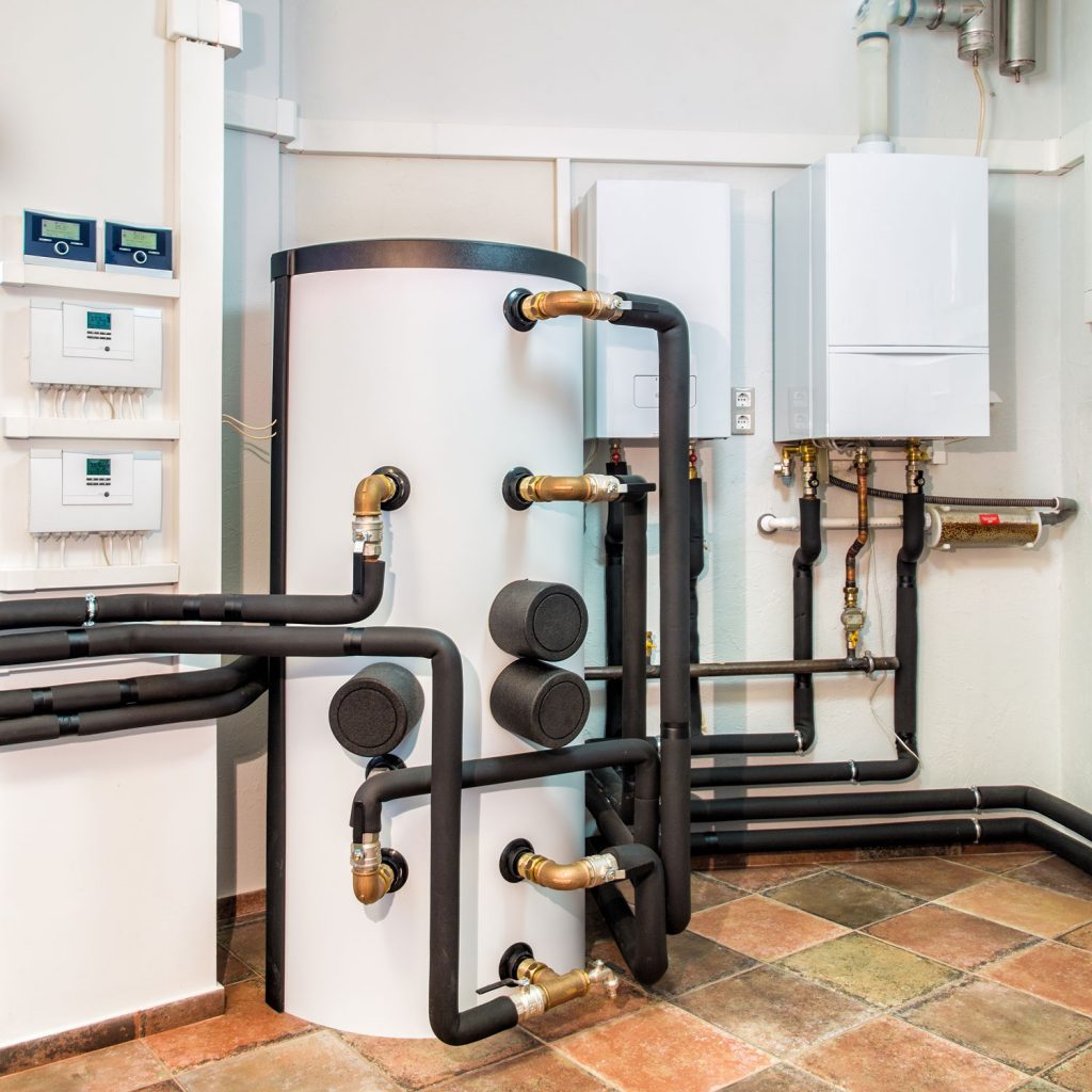 A huge white boiler with heavily insulated pipes and circuit breakers on the wall