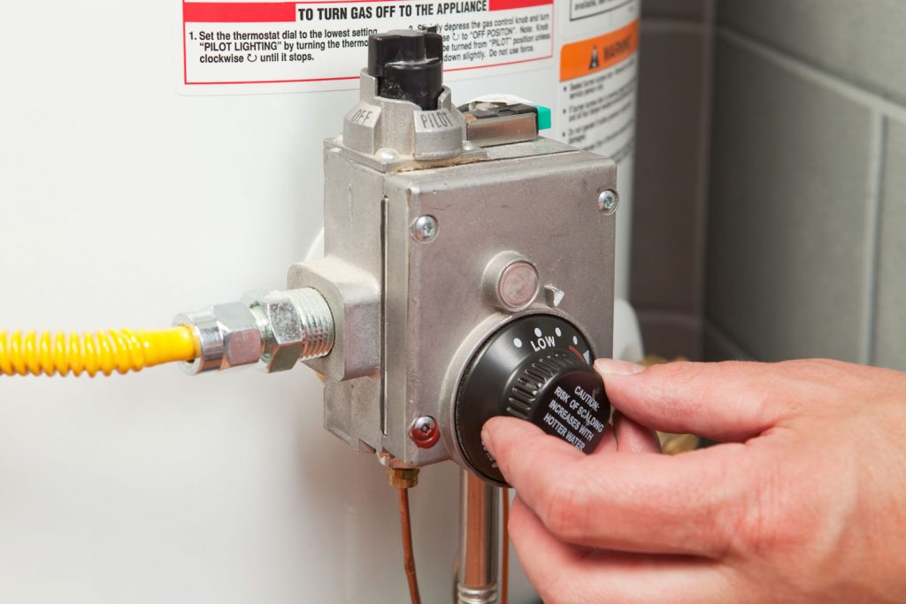A male hand is turning down the temperature on a gas water heater's thermostat