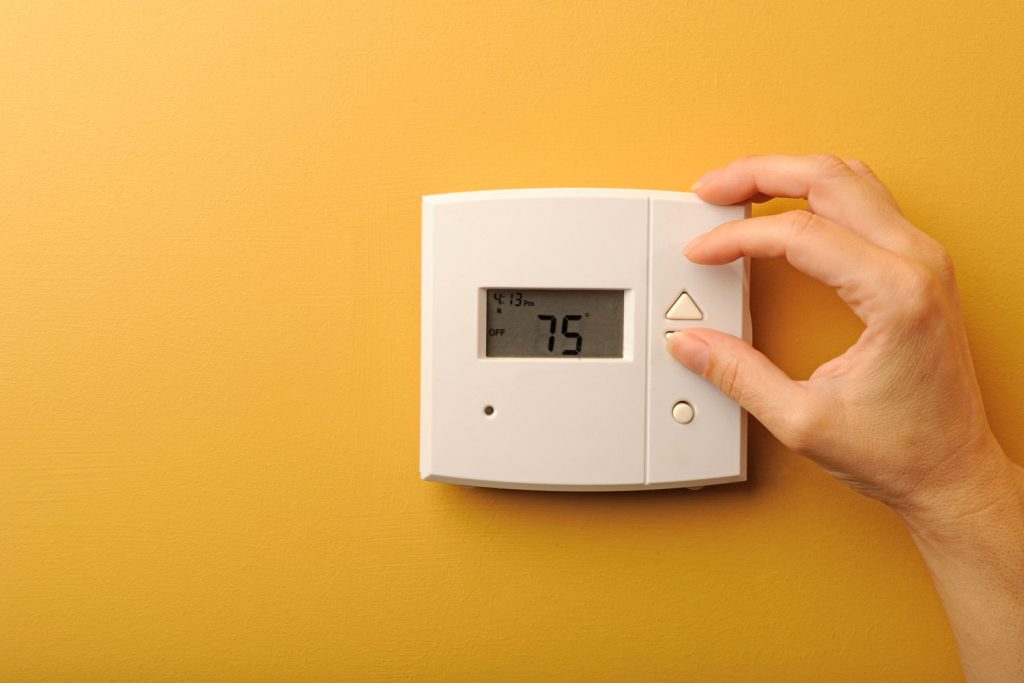 A man adjusting the thermostat mounted to a yellow painted wall