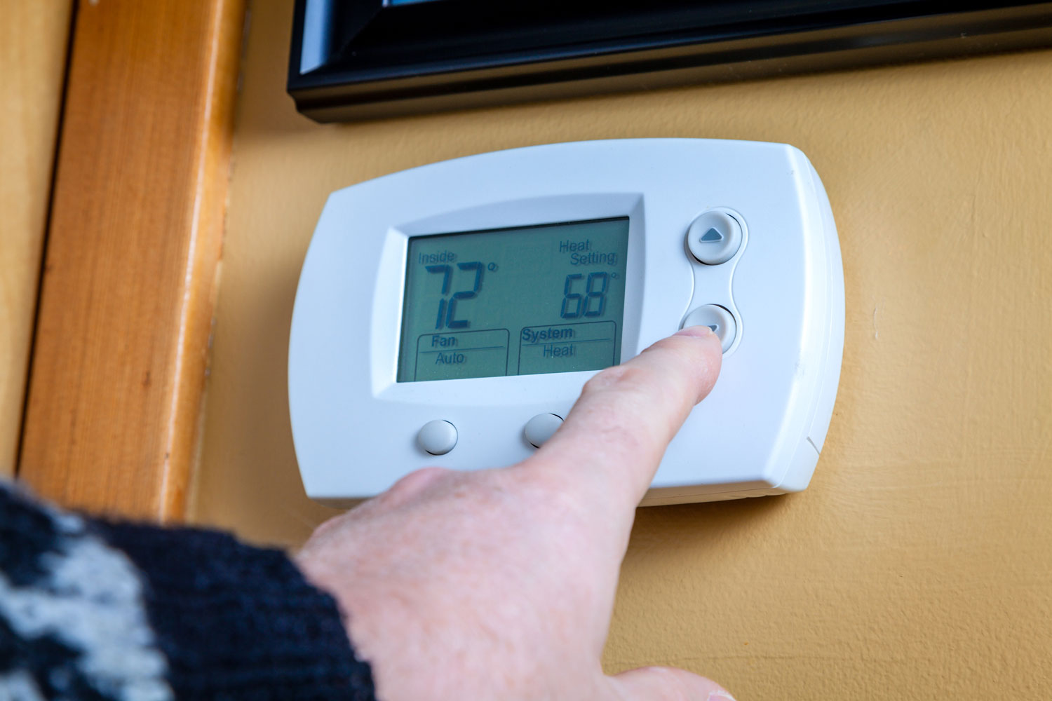 A person lowers temperature on a home thermostat. Enegry saving concept