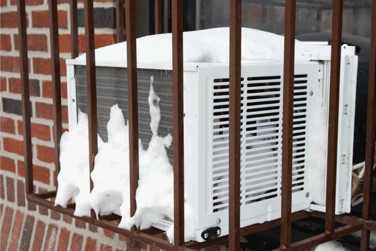 A-window-air-conditioner-in-a-barred-cage-with-snow-on-a-brick-urban-building.-Should-You-Remove-Window-Air-Conditioners-In-The-Winter