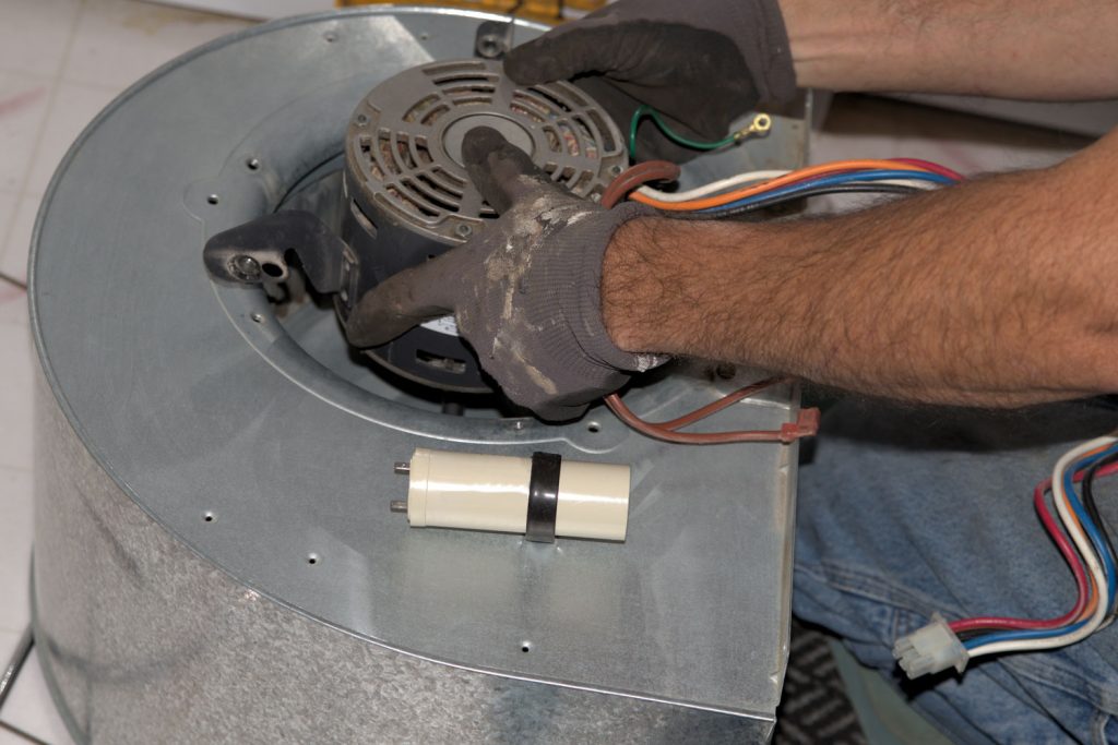 A worker installing a newly fixed furnace fan motor