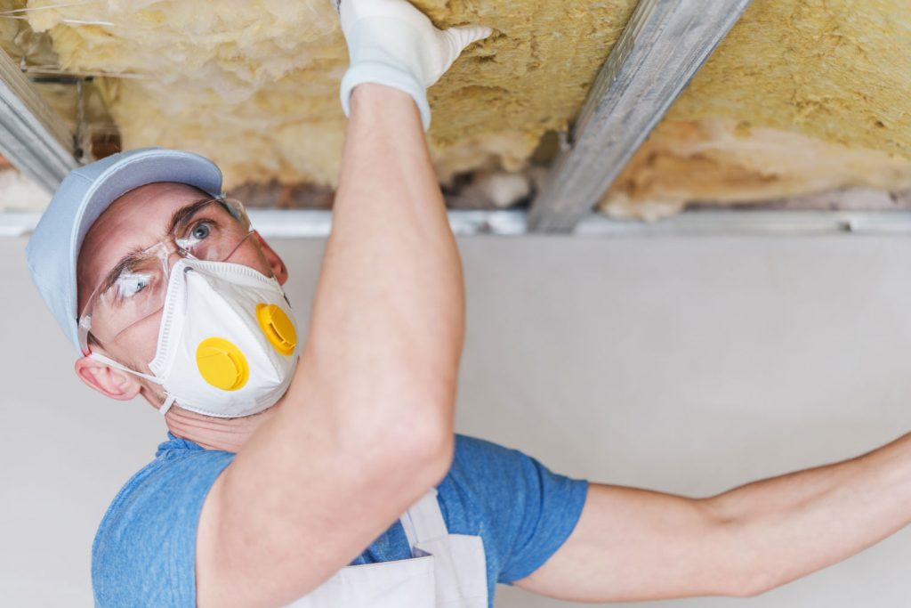 A worker installing insulation at the ceiling of a house