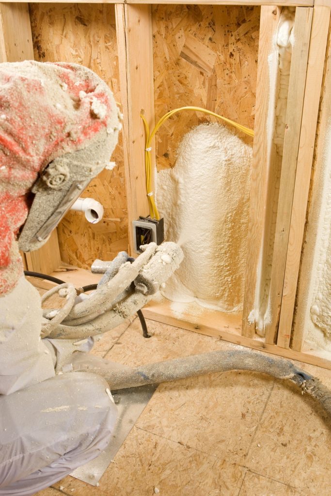 A worker spraying foam insulation to the foundation wall
