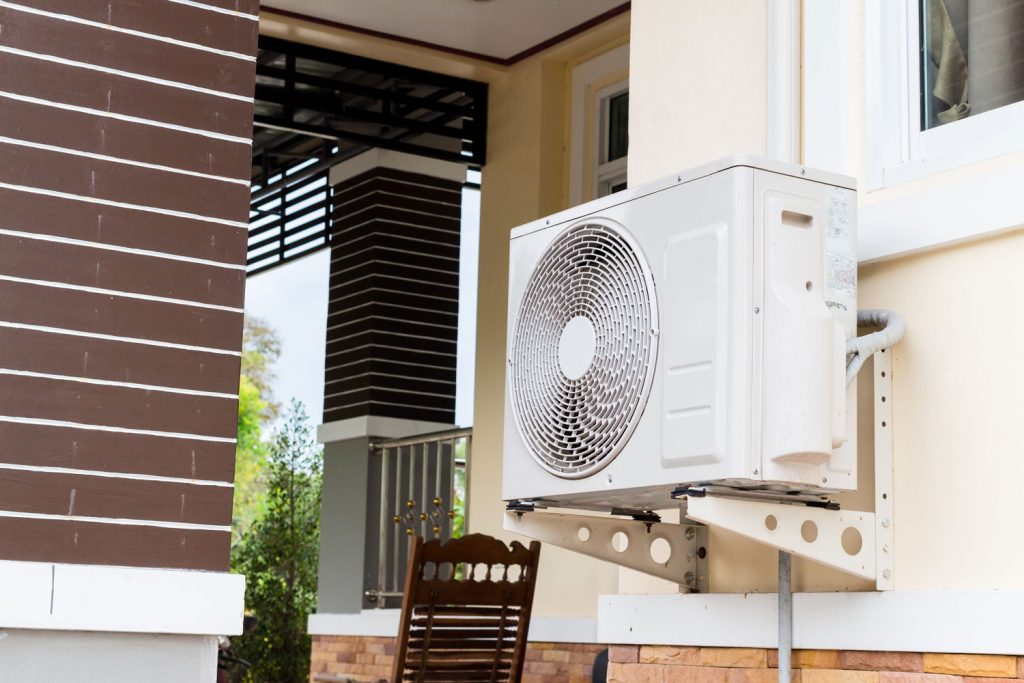 An air conditioning condenser unit installed outside a white painted house