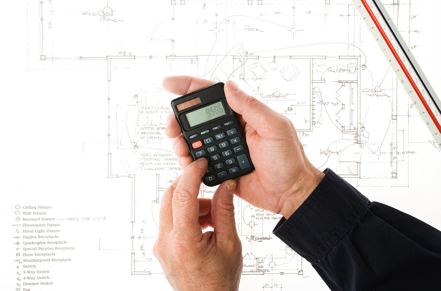 Contractor estimating the cost of a construction project with a calculator and a ruler over an architectural blueprin