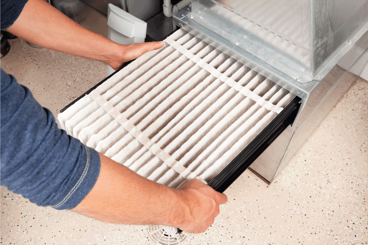 Male hands are installing a furnace air filter. This filter is not brand new but it is relatively clean, it was removed for inspection