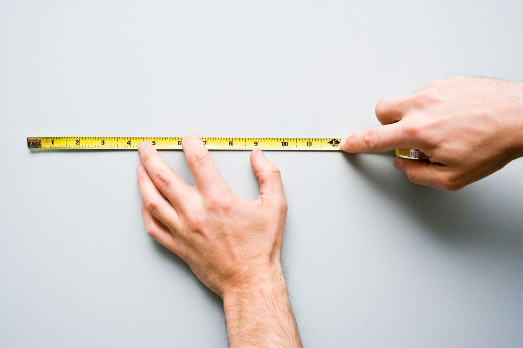Man stands holding measuring tape against the wall