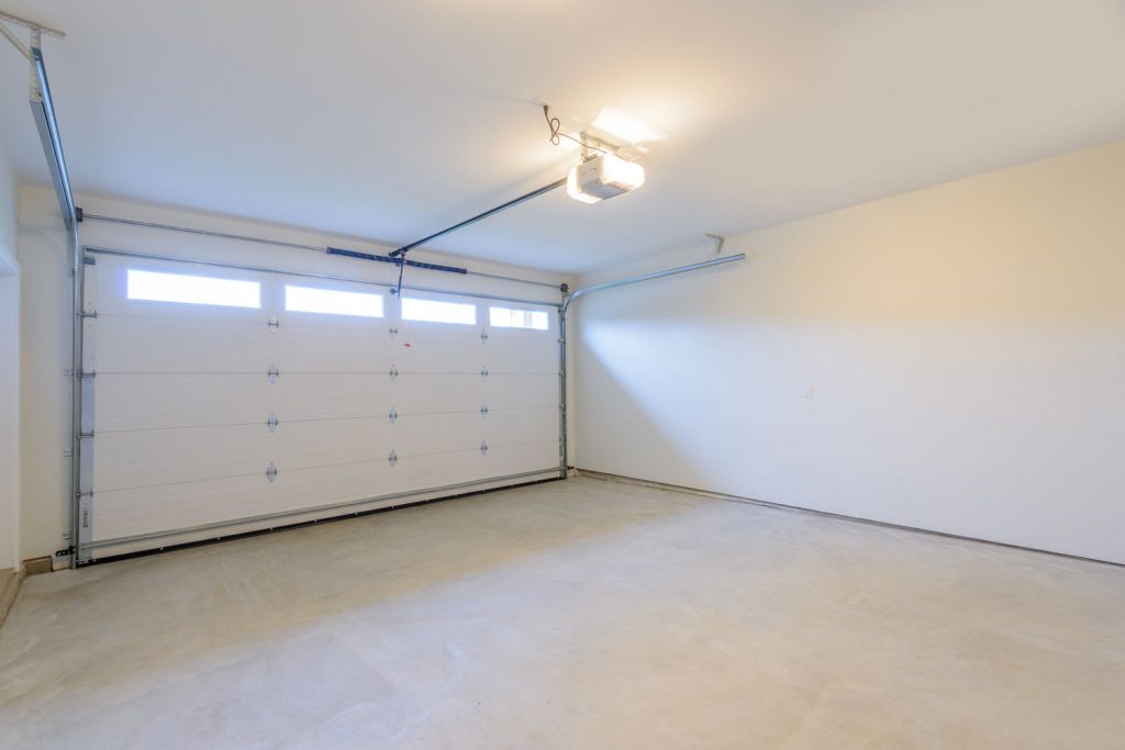 White and spacious garage with white walls painted concrete flooring and a light on the garage mechanism