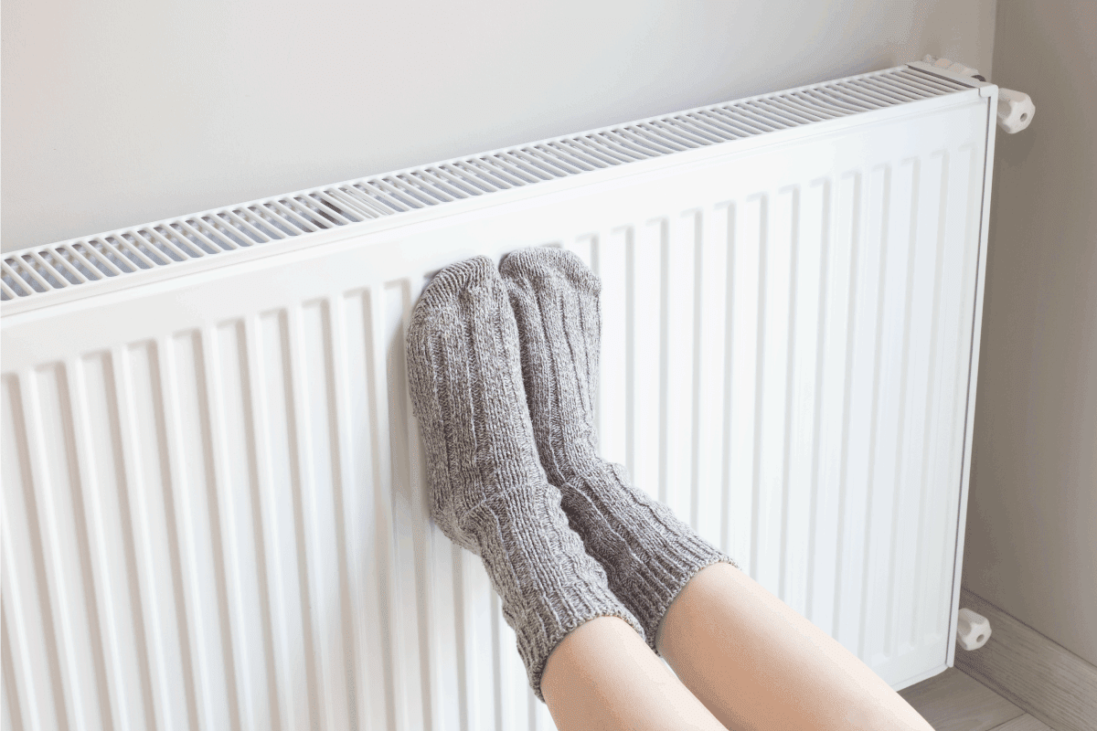 Woman is warm knitted woolen socks near a home heater in cold winter time. Using heater at home in winter. Do Furnaces Come With Dehumidifiers